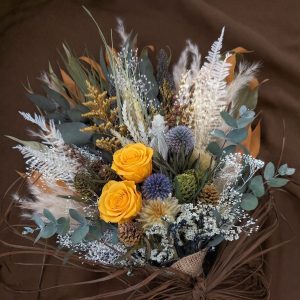 Runsaassa kuivakukkakimpussa kirkkaat keltaiset stabiloidut ruusut ja teräksensiniset sinipallo-ohdakkeet tuovat eloa neutraalien sävyjen ja eukalyptuksen keskelle.