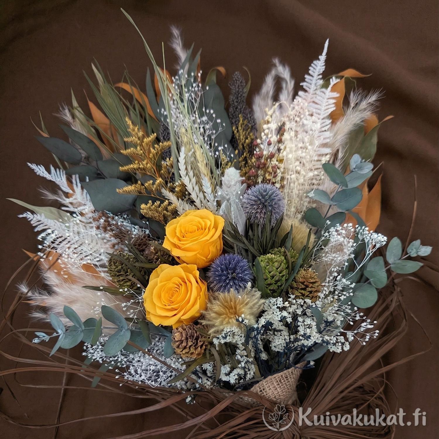 Runsaassa kuivakukkakimpussa kirkkaat keltaiset stabiloidut ruusut ja teräksensiniset sinipallo-ohdakkeet tuovat eloa neutraalien sävyjen ja eukalyptuksen keskelle.